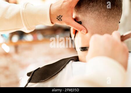 Crop anonyme coiffeur rasoir homme en masque avec rasoir droit en barbershop sur fond flou Banque D'Images