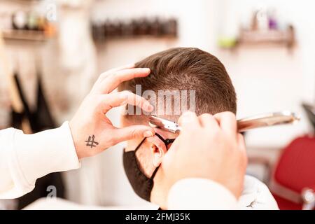 Crop anonyme coiffeur rasoir homme en masque avec rasoir droit en barbershop sur fond flou Banque D'Images