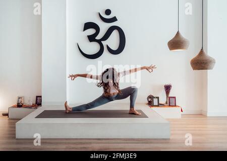 Femme mince en vêtements d'activité faisant du yoga sur tapis à Skandasana dans un studio spacieux Banque D'Images