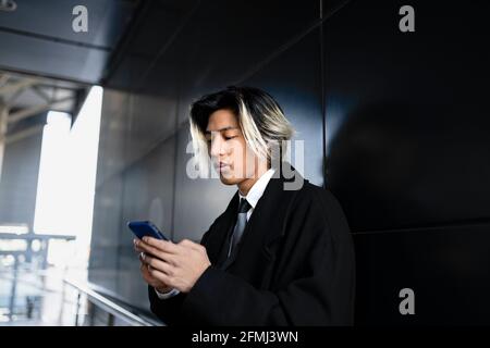 Jeune homme asiatique attentif dans les messages textes officiels de vêtements sur téléphone portable en plein jour Banque D'Images