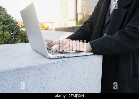 Écourté non reconnaissable bien habillé homme exécutif travaillant sur netbook contre bâtiments modernes de la ville Banque D'Images