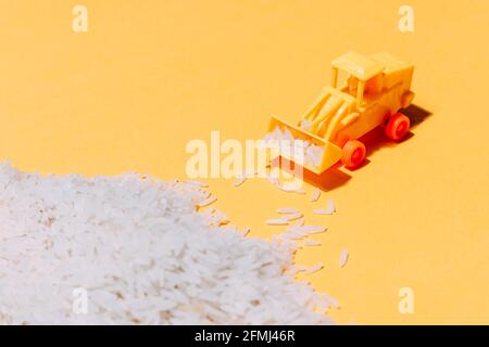 Par le dessus du petit tracteur en plastique en peluche qui recueille le tas de grains de riz éparpillés sur fond jaune Banque D'Images