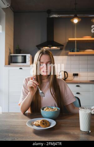 Jeune femme avec une cuillère et un bol pour déguster de savoureux anneaux de maïs dans la cuisine Banque D'Images