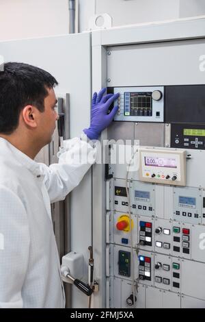 Crop concentré professionnel homme assistant de laboratoire en robe blanche et gants en latex appuyant sur les boutons de l'équipement moderne Banque D'Images