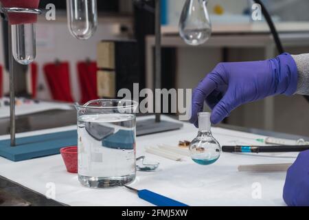 Crop scientifique anonyme en gants de protection secouant la substance chimique bleue en flacon tout en travaillant dans un laboratoire moderne équipé Banque D'Images