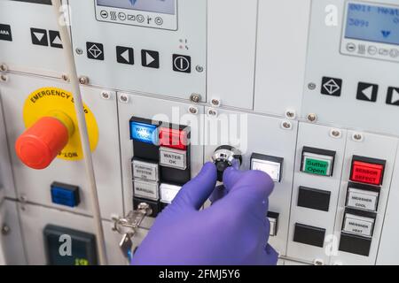 Rognez un assistant de laboratoire masculin professionnel non reconnaissable en robe blanche et gants en latex appuyant sur les boutons de l'équipement moderne Banque D'Images