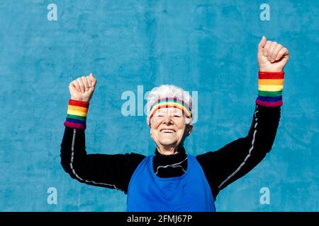 Femme sénior dans les vêtements de sport célébrant la victoire avec des poings serrés et bras levés sur fond bleu en studio Banque D'Images