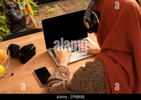 De dessus anonyme femelle dans le foulard à l'aide de netbook moderne avec écran noir assis au bureau Banque D'Images