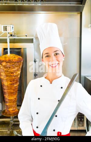 Döner Kebab - vendeur amical dans un restaurant fast food turc, avec un couteau en face de brochette Banque D'Images