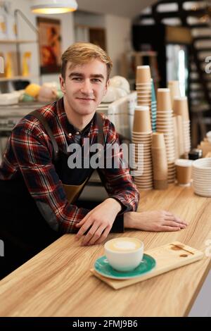 bon serveur dans un tablier tenant une tasse de boisson chaude Banque D'Images