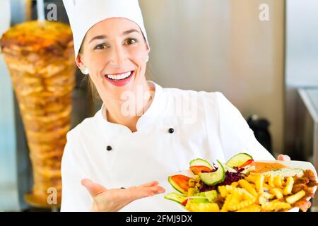 Döner Kebab - friendly female vendeur dans un restaurant fast food turc, maintenant la plaque avec frites et kebab en face de brochette Banque D'Images