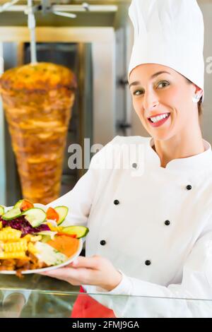 Döner Kebab - friendly female vendeur dans un restaurant fast food turc, maintenant la plaque avec frites et kebab en face de brochette Banque D'Images