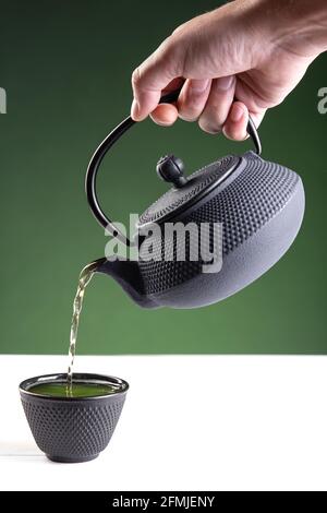 Eau versée dans une tasse sombre de thé vert sur fond vert avec espace de copie.format vertical. Banque D'Images