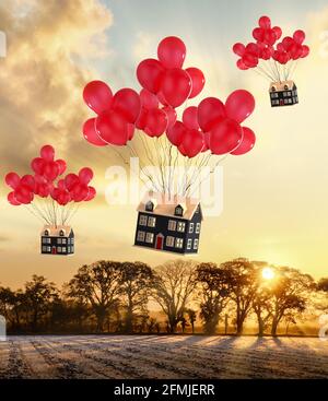 Maisons de jouets attachées à des ballons rouges volant au-dessus des champs ruraux. Passage au pays et aux concepts immobiliers Banque D'Images