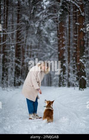 Une jeune femme blonde joue avec son corgi gallois pembroke dans une forêt enneigée d'hiver. Banque D'Images