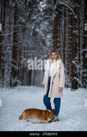 Une jeune femme blonde joue avec son corgi gallois pembroke dans une forêt enneigée d'hiver. Banque D'Images