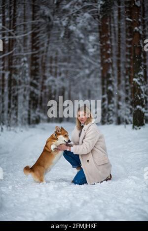 Une jeune femme blonde joue avec son corgi gallois pembroke dans une forêt enneigée d'hiver. Banque D'Images