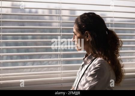 Jeune femme latine médaillée thérapeute debout à la fenêtre avec le sourire Banque D'Images