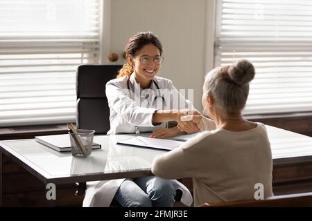 Jeune femme hispanique médecin secouer la main de femme âgée patient Banque D'Images