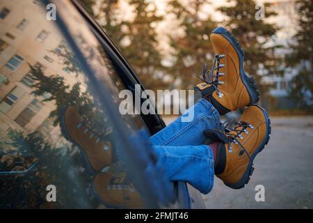 Femme pieds dans des bottes de randonnée jaune tendance sur la porte de voiture. Pieds à l'extérieur de la fenêtre au coucher du soleil forêt. Le concept de liberté de mouvement. Un week-end d'automne Banque D'Images