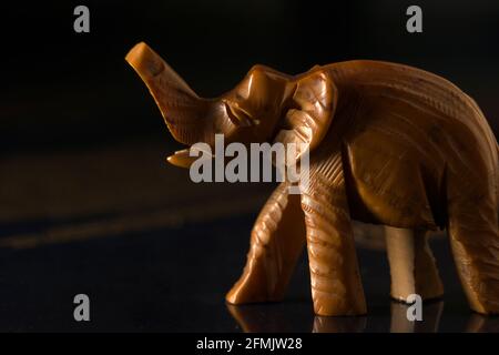 Gros plan d'une figure en bois sculpté d'un éléphant avec un tronc relevé au sommet. Éléphant jouet sur fond sombre. Foyer extrême sélectif Banque D'Images