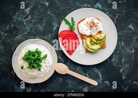 Griller avec des œufs pochés, des graines de lin, des tranches d'avocat et de tomate et du fromage cottage avec des feuilles d'arugula coupées sur une assiette. Repas sain pour le petit déjeuner. Banque D'Images