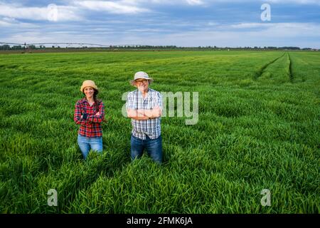 Deux générations de fermiers fiers sont debout dans leur champ d'orge au coucher du soleil. Banque D'Images