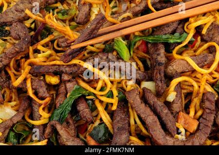Les nouilles au bœuf et aux œufs sautés avec des légumes et du bois arrière-plan des baguettes Banque D'Images