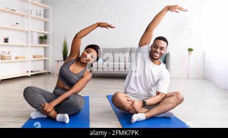 Sports domestiques. Couple noir sportif en vêtements de sport faire des exercices de remise en forme sur tapis de yoga à la maison, panorama. S'adapte au jeune homme et à sa petite amie Banque D'Images