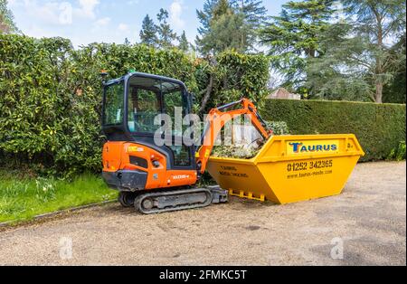 Un véhicule à chenilles en caoutchouc, une minipelle Kubota KX016-4 orange et un saut jaune utilisé pour le dégagement du jardin et l'enlèvement des débris, Surrey, Angleterre Banque D'Images