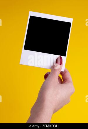 femme main tenant le cadre photo instant pack film polarioïde avec insérer la carte sur fond jaune Banque D'Images