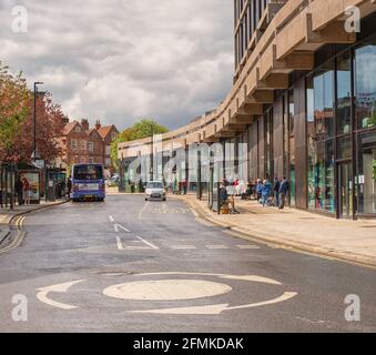 Des abris de bus bordent une rue humide juste après une douche à effet pluie. Un bâtiment moderne en verre se courbe avec la rue et un bus attend par un arrêt. Banque D'Images