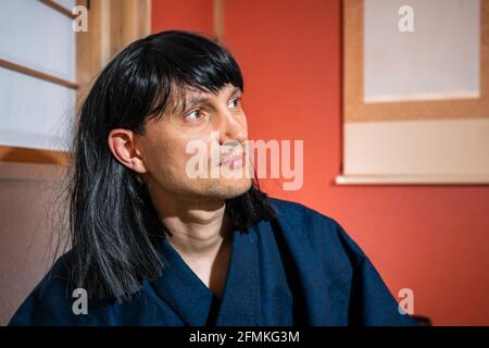 Intérieur japonais traditionnel avec homme en costume kimono et cheveux noirs assis par alcôve suspendre papier rouleau avec noir perruque de cheveux Banque D'Images