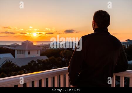 Vue aérienne à grand angle sur un coucher de soleil coloré avec un homme regardant la vue sur le golfe du Mexique à Seaside, Floride sur le bâtiment terrasse balcon roo Banque D'Images