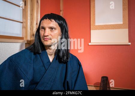 Chambre japonaise traditionnelle intérieure avec homme face i n kimono costume et cheveux noirs assis à côté d'alcôve pendante rouleau de papier perruque à cheveux noirs Banque D'Images