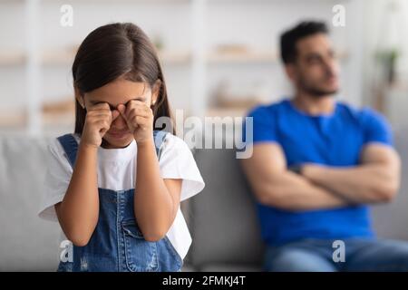 Problèmes de relations familiales. Un accent sélectif sur les pleurs offensés petite fille fille essuyant des larmes, jeune père assis séparément sur le canapé dans le b flou Banque D'Images