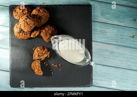 Biscuits au chocolat avec raisins secs et une tasse de lait sur une assiette noire. Vue de dessus, plat. Banque D'Images