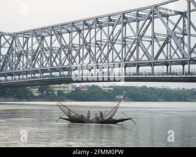 KOLKATA, INDE - 08 mai 2021 : deux hommes dans une rangée de bateaux traditionnelle à travers la rivière Hoogly avec le pont Howrah à l'arrière-plan pour les poissons Banque D'Images