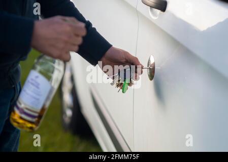 Ivre en charge d'un camping-car. Un homme déverrouille la porte de sa camionnette avec une bouteille d'alcool de whisky dans sa main. Buvez conduire Angleterre Royaume-Uni Banque D'Images