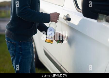 Ivre en charge d'un camping-car. Un homme déverrouille la porte de sa camionnette avec une bouteille d'alcool de whisky dans sa main. Buvez conduire Angleterre Royaume-Uni Banque D'Images