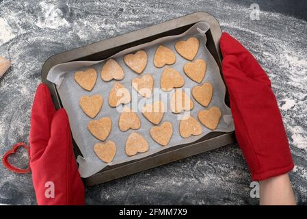 Chef dans les mitaines de four contenant des biscuits fraîchement cuits en forme de coeur Banque D'Images
