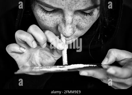 Drogue Addict renifler et ronfler la cocaïne, vitesse, héroïne ou autre drogue avec l'argent roulé sur le miroir avec fond sombre, toxicomanie, drogues, déprimé Banque D'Images