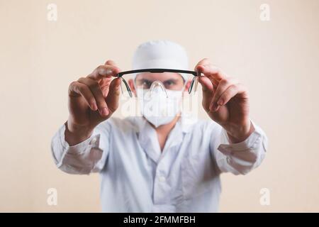 Lunettes de protection chez les médecins mains en blouse de laboratoire blanche et masque respiratoire protecteur défoqué sur fond jaune isolé. Mise au point sélective. Banque D'Images
