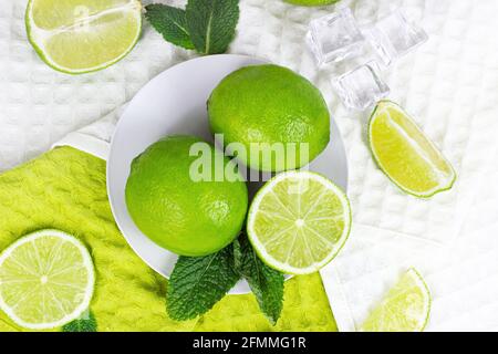 Vue de dessus des limes vertes fraîches juteuses et des tranches de citron vert avec feuilles de menthe dans la cuisine sur fond clair. Banque D'Images