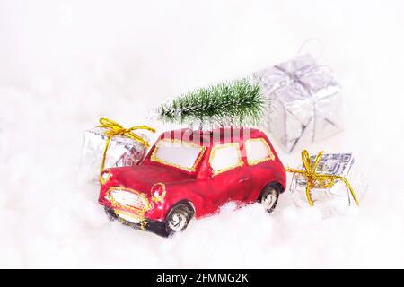 Petite voiture rouge rétro avec sapin vert sur le dessus et présente sur fond blanc de neige artificielle. Fête de Noël et du nouvel an Banque D'Images