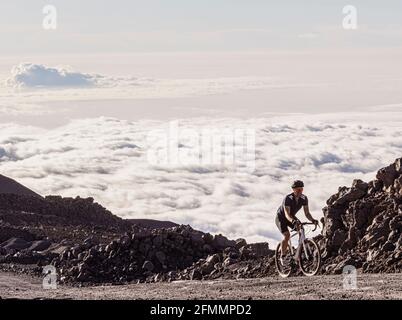 Un cycliste se promère sur une route de gravier au-dessus des nuages sur Mauna Kea, à Hawaï Banque D'Images