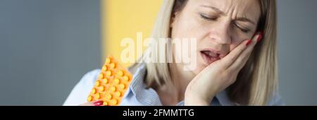 La femme souffre de maux de dents et tient des pilules dans ses mains Banque D'Images