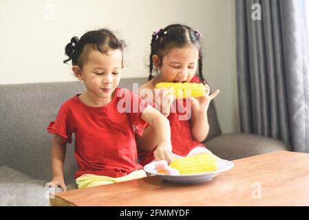 Petite fille jouant et mangeant du maïs à la maison, asiatique mignon fille heureux enfants concept alimentaire Banque D'Images