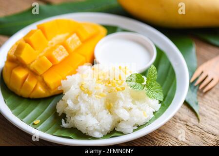 Riz à la mangue mûr cuit avec du lait de coco, dessert thaï asiatique, zeste de mangue douce tropicale et coupé en tranches sur une assiette blanche et des feuilles de menthe fraîche, Mango sticky r Banque D'Images