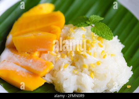 Riz mûr à la mangue cuit avec du lait de coco, dessert thaï asiatique, zeste de mangue douce tropicale et coupé en tranches de haricots jaunes sur la feuille de banane et le congé de menthe fraîche Banque D'Images